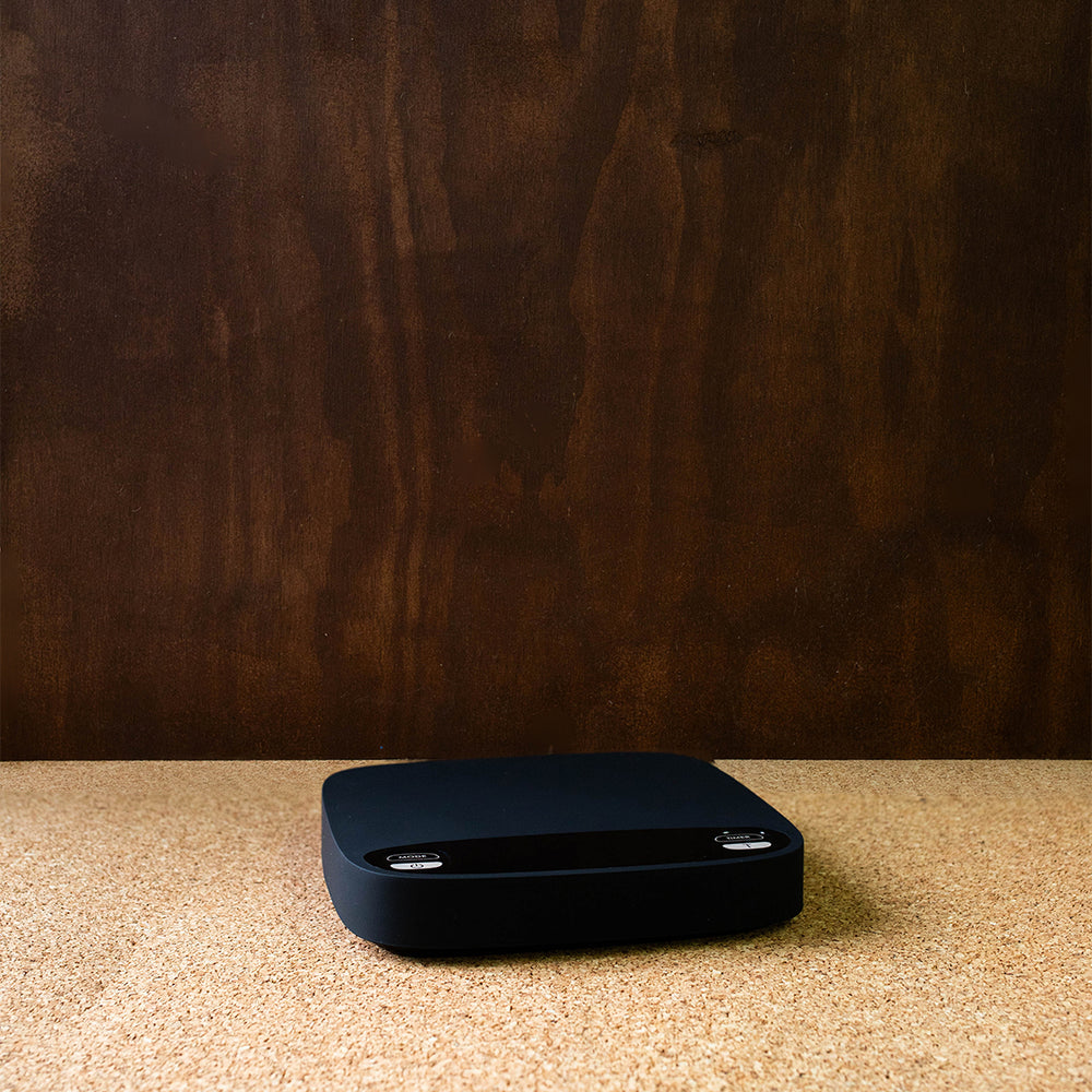 A black Brewace digital coffee scale placed on a wooden surface, displaying a clean and simple design with a large LED screen.